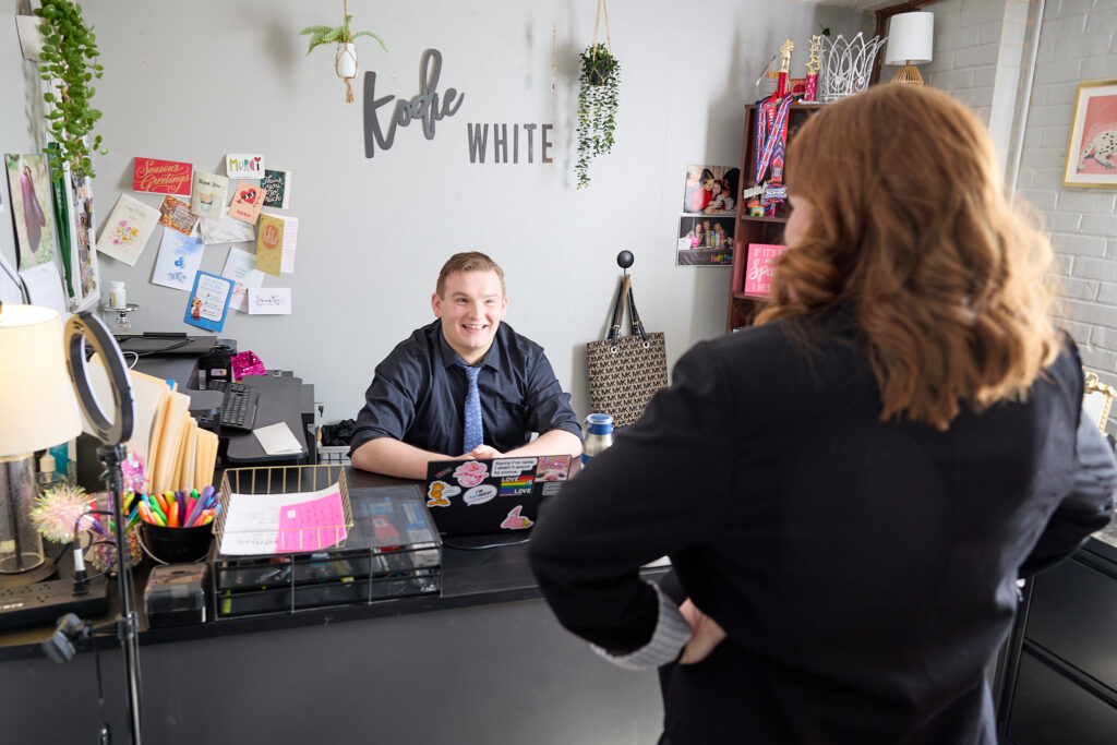 Health Plus Indiana team member welcoming a colleague at the front desk of the Pride-decorated office.